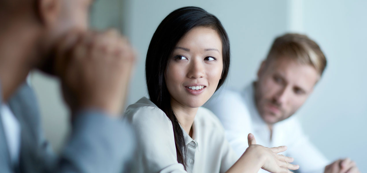 Two men looking at a woman sitting between them while she speaks during a meeting.